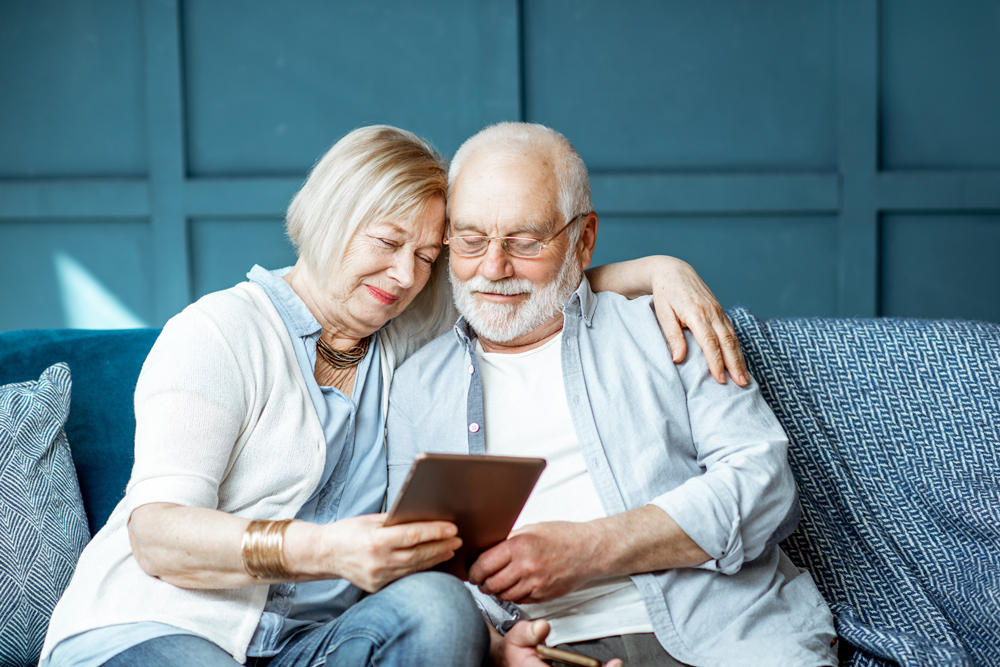 Lovely senior couple dressed casually using digital tablet while sitting together on the comfortable couch at home
