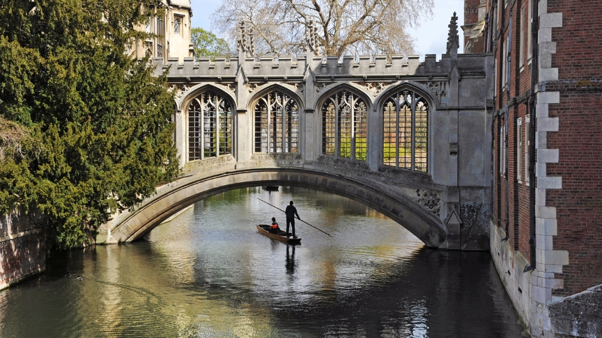 A person standing on a boat punting down the river in Cambridge about to go under a beautiful historic bridge