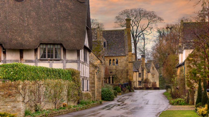 View of a quaint countryside street in the Cotswolds with thatched-rooved cottages and houses built with Cotswold stone