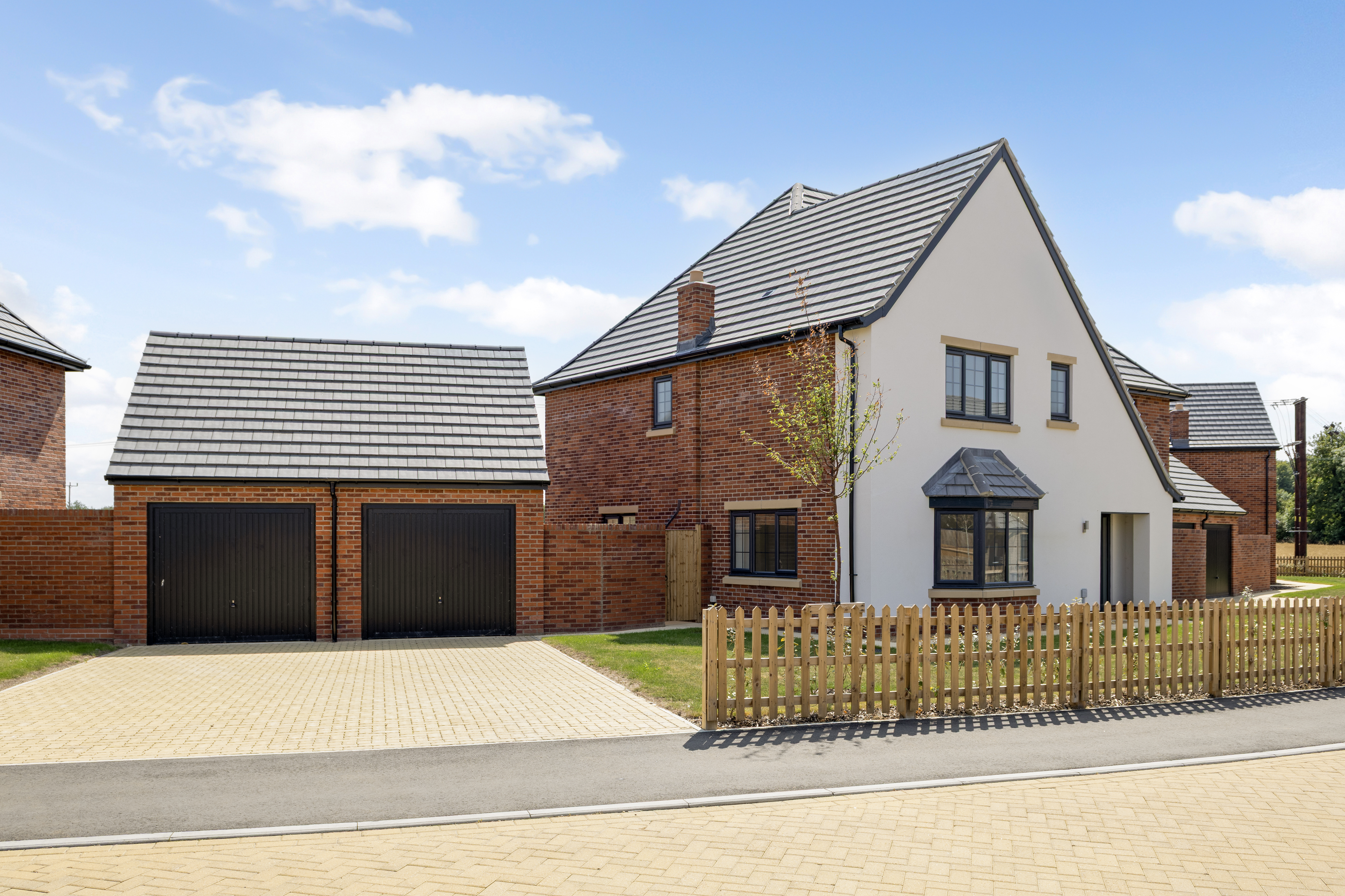  Stylish newly built two-story home with red brick and white exterior, grey tiled roof, and large windows. Includes a detached double garage, paved driveway, and wooden picket fence.
