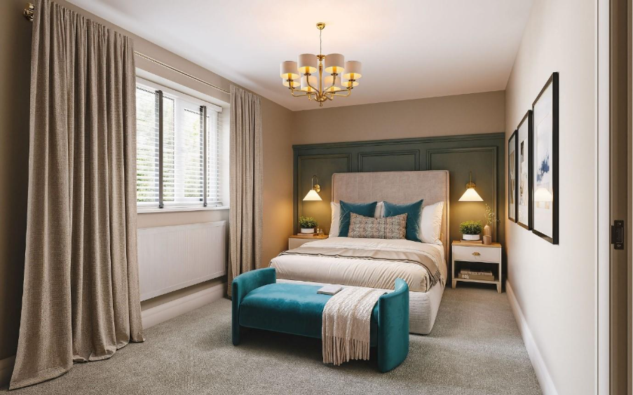 A modern, softly lit bedroom with a double bed centred against a green panelled feature wall. The bed has neutral bedding with teal cushions and a matching teal bench at the foot. Two bedside tables with warm pendant lights sit on either side. Large curtains frame a window on the left, and framed artwork hangs on the right wall.