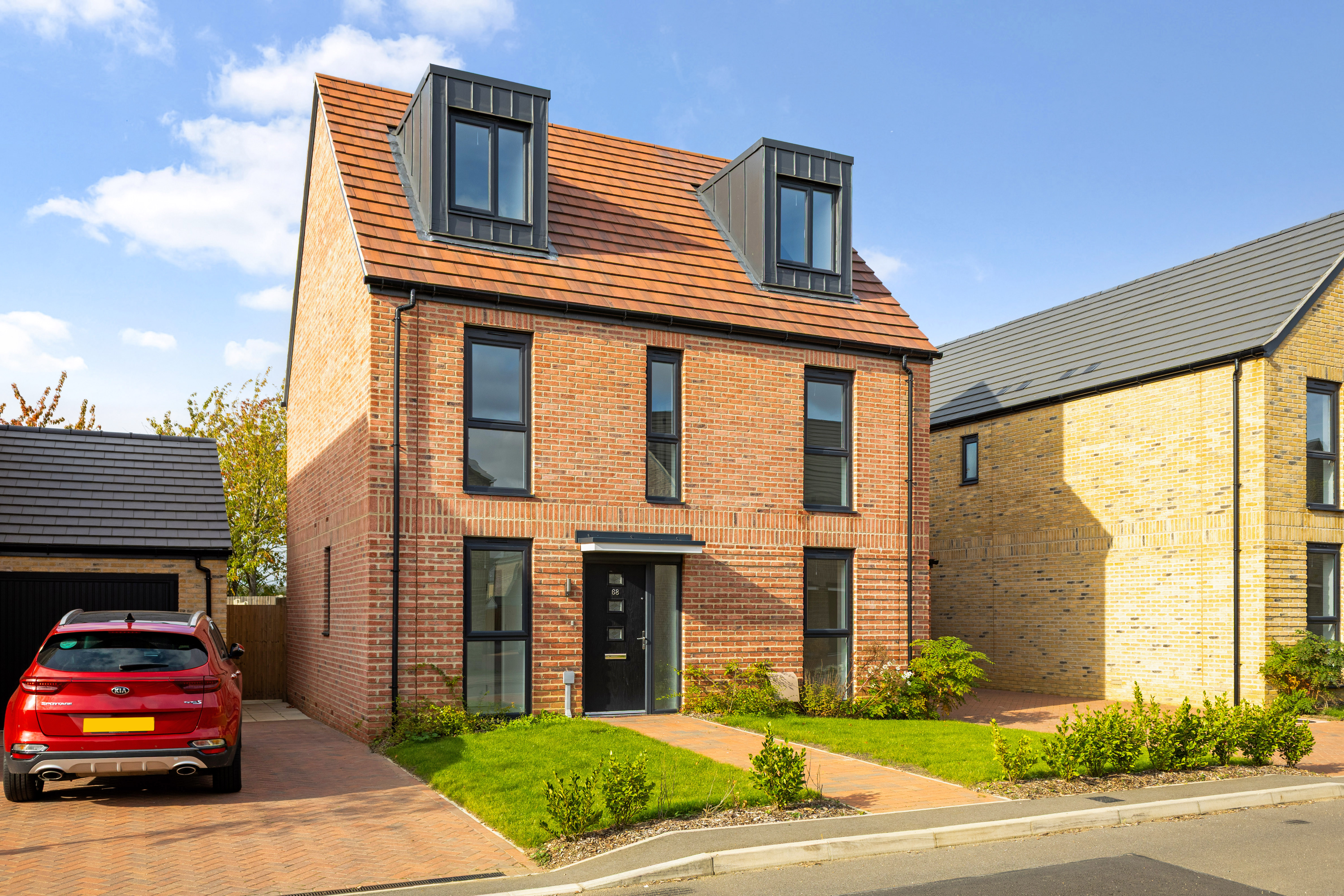 New-build three-storey red brick detached house with dormer windows, private driveway, and landscaped front garden.