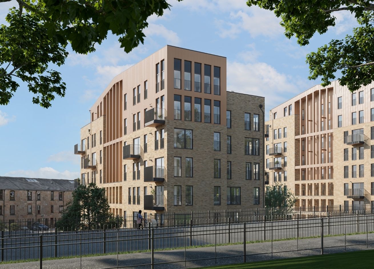Modern residential complex with light brick and wood-panelled buildings, large windows, trees, and a person walking on the pavement.