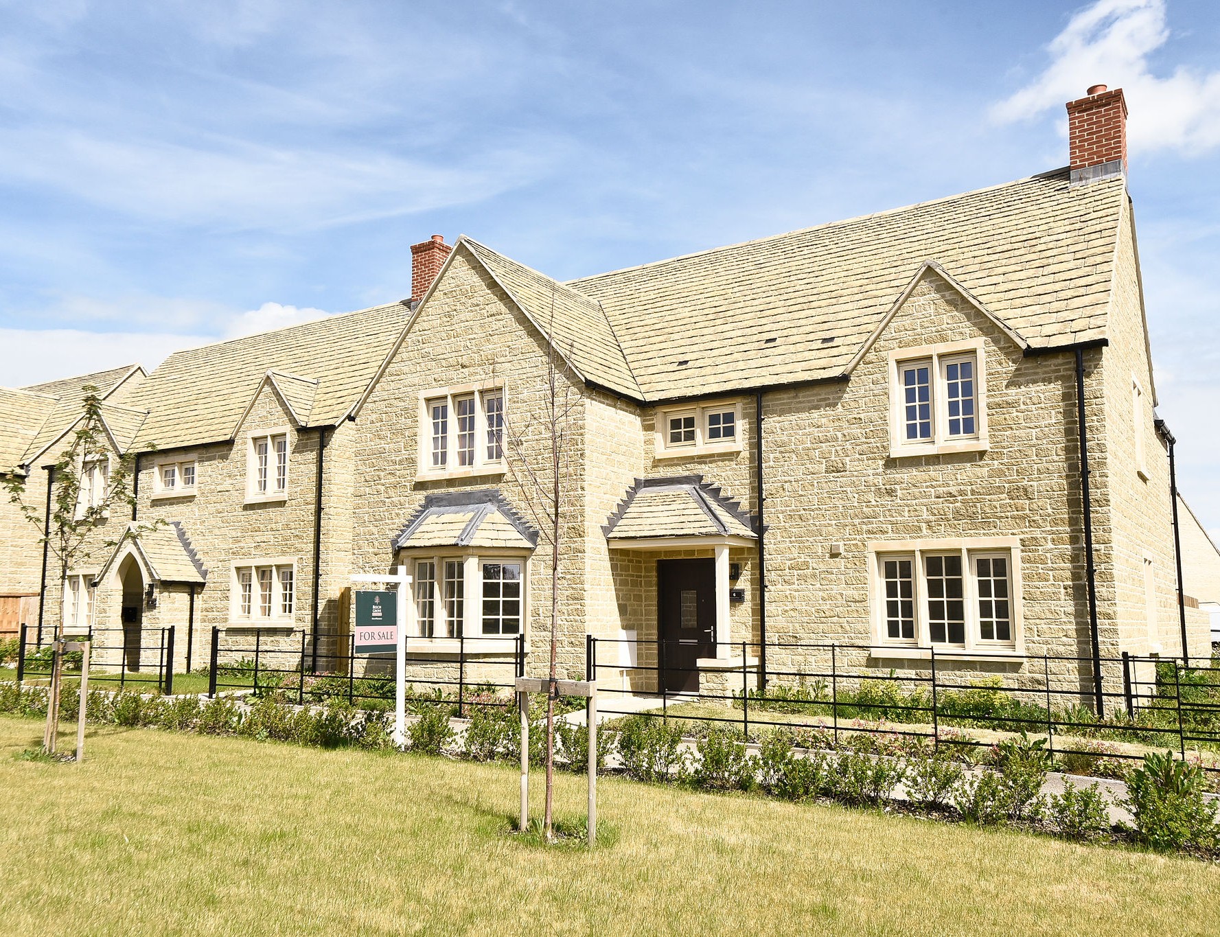 Large Cotswold stone property, with black railings, landscaped grass and blue sky