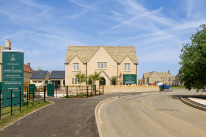 Brand new houses in Cotswold stone, on a sunny day. With signage at the entrance with open green space and plants