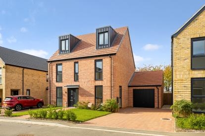 Two‑storey red brick detached house with pitched roof, front garden, driveway and separate garage, on a modern residential street.