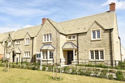 Large Cotswold stone property, with black railings, landscaped grass and blue sky
