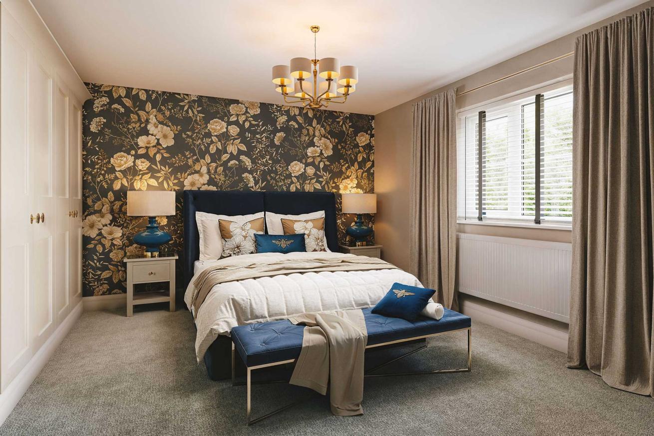 Modern master bedroom with a large bed dressed in neutral tones, a padded headboard, bedside tables with lamps, a cushioned bench, and a round accent chair, complemented by beige walls and a wide window with curtains.