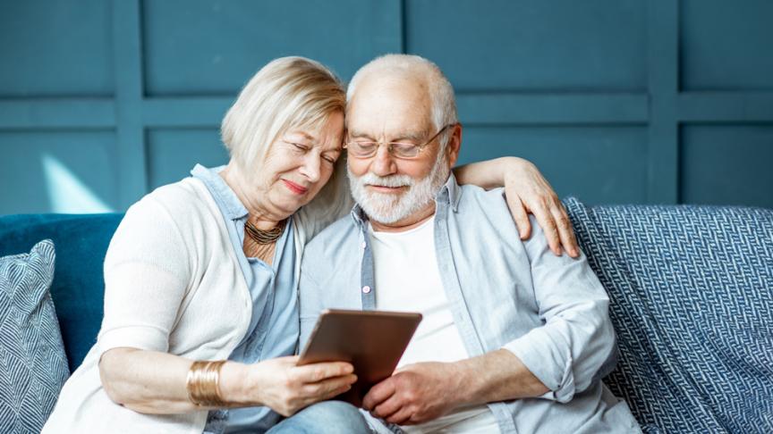 Lovely senior couple dressed casually using digital tablet while sitting together on the comfortable couch at home