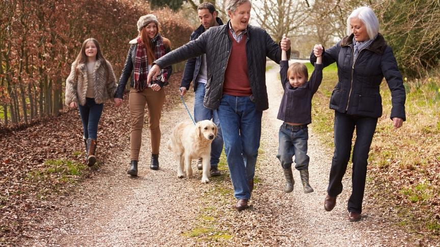 Happy grandparents, parents and children walking along a country road on an autumnal day, dressed up warm in coats and wellies with a golden retriever alongside them