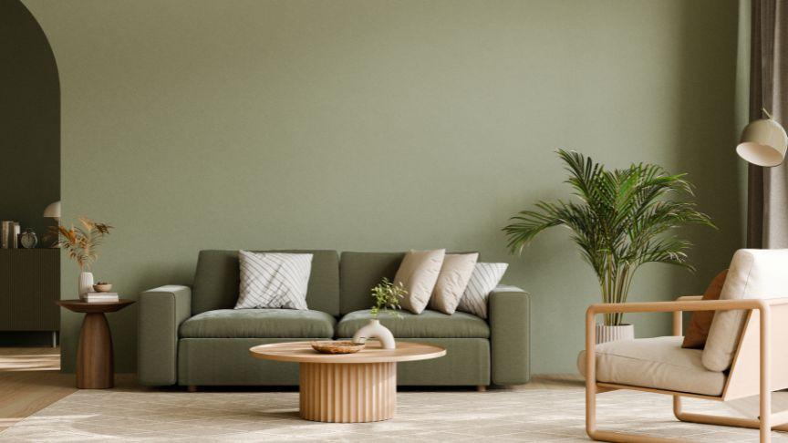 ere’s a short alt text for the image:  "Modern living room with green sofa, wooden coffee table, armchair, and large potted plant against a green wall