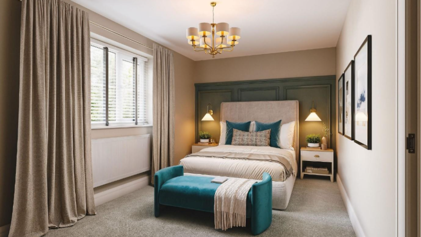 A modern, softly lit bedroom with a double bed centred against a green panelled feature wall. The bed has neutral bedding with teal cushions and a matching teal bench at the foot. Two bedside tables with warm pendant lights sit on either side. Large curtains frame a window on the left, and framed artwork hangs on the right wall.