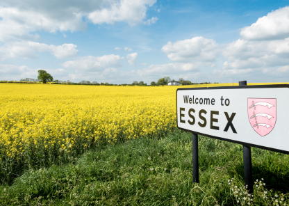 A sign in front of a large field of blooming yellow rapeseed which reads Welcome to Essex